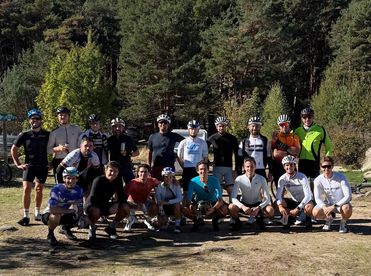 Grupo del club posando con casco y maillots en un pinar, con el cielo azul de fondo